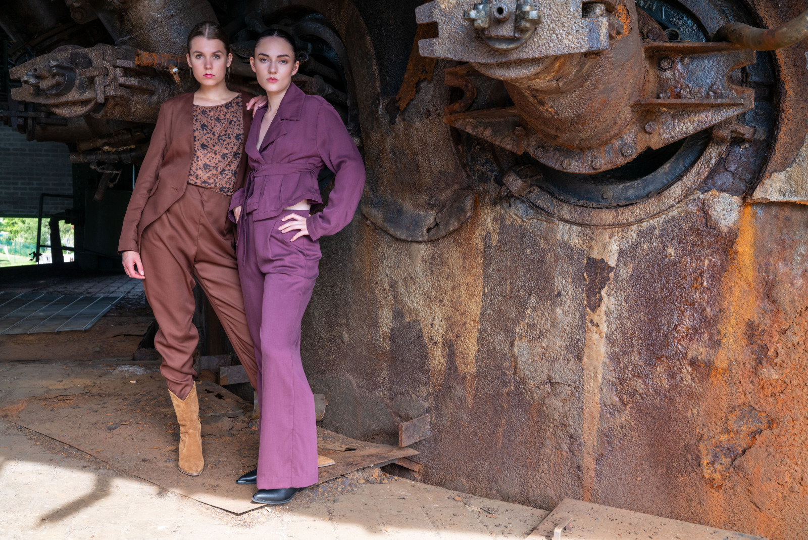 Hannah und Rosanna im herbstlichen Look, wie gemalt zu der stählernen Kulisse der Henrichshütte am alten Hochofen. Der ist der älteste Hochofen im Revier, ragt 55 Meter hoch und hat 80 Jahre auf dem Buckel. Zur Blütezeit arbeiteten 10.000 Menschen in dem Werk nahe der Ruhr, seit der schrittweisen Stilllegung ab 1987 wandelte es sich zum Museum, zeigt Relikte der Hüttenzeit, wie gewaltige Gasmaschinen im historischen Gebläsehaus und Natur auf der Industriebrache in Hattingen. Das Herbst-Outfit schmiegt sich in die Kulisse ein: Rosanna im roten Anzug aus Tencel und Hannah im braunen Anzug, das Material Rewoven und GOTS zertifiziert, mit Blusen-T-Shirt in Krepp aus Öko-Baumwolle.